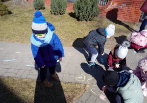 Dzieci w ogrodzie przedszkolnym malują kredami po chodniku